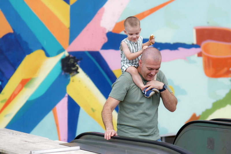 13 - Man holding a child on his shoulders in front of a colorful, abstract mural